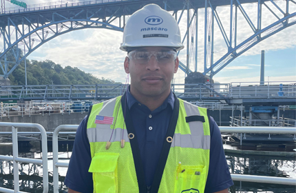 Young man in hard hat and safety vest in front of construction site